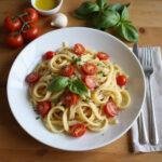 Budget-friendly dinner with pasta, cherry tomatoes, basil, garlic, and olive oil on a wooden table.