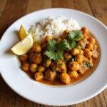 Vegan chickpea curry with rice, garnished with herbs and lemon, a filling and inexpensive meatless meal.