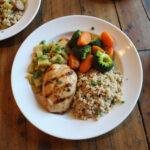 Healthy comfort food plate with grilled chicken, vegetables, and quinoa on wooden table.