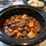 Slow cooker with beef stew and vegetables cooking, highlighting budget-friendly meal preparation.