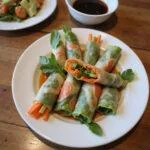 Fresh spring rolls filled with vegetables and herbs served with dipping sauce on a wooden table.