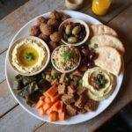 A vibrant Mediterranean mezze platter with hummus, falafel, tabbouleh, stuffed grape leaves, olives, and pita bread on a wooden table.