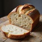 Freshly baked sourdough bread with a golden crust on a wooden table, showcasing its airy interior.