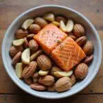 Close-up of a bowl of mixed nuts and a salmon fillet on a wooden table, emphasizing omega-3-rich foods beneficial for brain health
