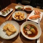 A traditional Japanese meal with sushi, tempura, miso soup, and chopsticks on a wooden table.