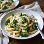 A plate of healthy broccoli pasta with green broccoli florets and pasta in a creamy sauce, garnished with cheese and herbs, presented on a wooden table in a cozy home environment.