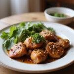 A serving of healthy sesame chicken plated on a dinner plate with sesame seeds and herbs, displayed in a home dining setting with warm lighting and a cozy atmosphere.