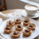 A plate of No-Bake Peanut Butter Oat Cups on a cozy home kitchen table, with sunlight streaming through a window, surrounded by a warm blanket and a coffee cup, in a warm and inviting setting.
