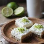 A realistic photo of chia pudding bars with coconut and lime flavor, presented on a rustic plate in a cozy kitchen setting, decorated with lime zest and shredded coconut for a refreshing look.