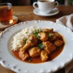 A plate of slow cooker chicken curry with rice, garnished with herbs, showcased on a cozy home dinner table, emphasizing warm lighting and homely decor.