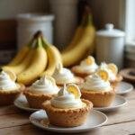 Close-up of mini banana cream pies on a cozy kitchen counter, featuring whipped topping and banana slices, with fresh bananas and whipped cream nearby for a warm, inviting scene.