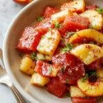 A vibrant summer salad featuring juicy peach slices and fresh watermelon cubes garnished with mint leaves on a white plate