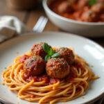 A plated baked spaghetti and meatballs dish with baked meatballs and spaghetti in a rich tomato sauce, garnished with herbs, presented on a plate on a cozy home dining table.