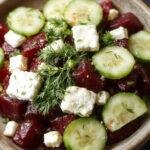 A vibrant beet salad featuring freshly sliced beets, crumbled feta cheese, crisp cucumber slices, and fresh dill sprinkled on top, served on a white plate.