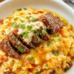 A bowl of creamy queso rice topped with tender grilled steak strips and fresh herbs, garnished with lime wedges and cilantro.