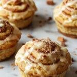 A close-up of freshly baked cinnamon roll muffins with swirls of cinnamon and icing topping, arranged on a rustic plate.