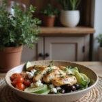 Realistic image of a Mediterranean chicken bowl served in a cozy home kitchen with grilled chicken, cherry tomatoes, cucumber, olives, feta cheese, and herbs on a wooden table.