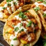 A plate of vibrant fried chicken street corn tacos topped with chopped cilantro and jalapeño lime ranch drizzle, served on a colorful background.