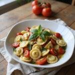 Close-up of Italian Tortellini Pasta Salad on a white plate with fresh vegetables and basil, styled on a wooden table in a cozy home environment, showcasing a colorful and appetizing dish.