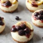 Mini Lemon Blueberry Cheesecakes with tart lemon slices and fresh blueberries on top, displayed on a white plate.