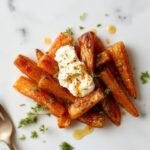 A beautifully plated dish of roasted carrots topped with creamy whipped ricotta and drizzled with warm hot honey, garnished with fresh herbs.