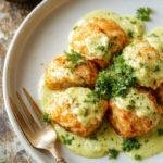 Close-up of golden salmon balls served with a vibrant, creamy avocado sauce drizzled on top, garnished with fresh herbs.