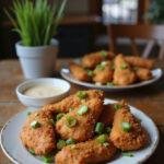Realistic image of salt and pepper crispy chicken on a plate in a cozy home setting, with golden, crispy chicken pieces garnished with green onions and pepper, accompanied by a dipping sauce.