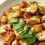 A vibrant plate of Thai Basil Chicken featuring stir-fried chicken, fresh basil leaves, red chili peppers, and jasmine rice garnished with lime slices.