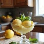 A refreshing lemon basil sorbet in a glass bowl, garnished with basil leaves and lemon slices, displayed on a cozy kitchen countertop with warm natural light and rustic kitchen elements.