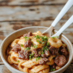A colorful bowl of Mongolian ground beef noodles featuring tender beef crumbles, glossy sauce, vibrant green scallions, and perfectly cooked noodles, styled in a rustic white bowl on a wooden surface with fresh ingredients around.