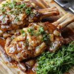 Golden-brown seared pork chops resting on a bed of caramelized onions and red bell peppers in a baking dish, drizzled with rich brown gravy, garnished with fresh parsley, served alongside creamy mashed potatoes in a rustic ceramic bowl on a wooden table.