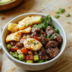 A vibrant Mediterranean steak bowl served in a white ceramic bowl: seared strip steak sliced over quinoa, topped with cherry tomatoes, cucumber, kalamata olives, red onion, crumbled feta, and fresh parsley, drizzled with olive oil and lemon wedges on the side.